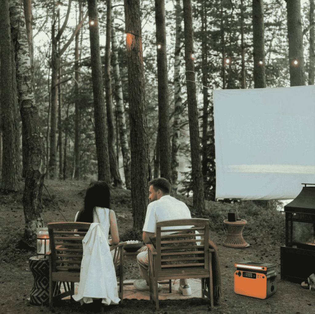  Estación de energía solar portátil alimentando una pantalla de cine y luces en un bosque durante la noche.