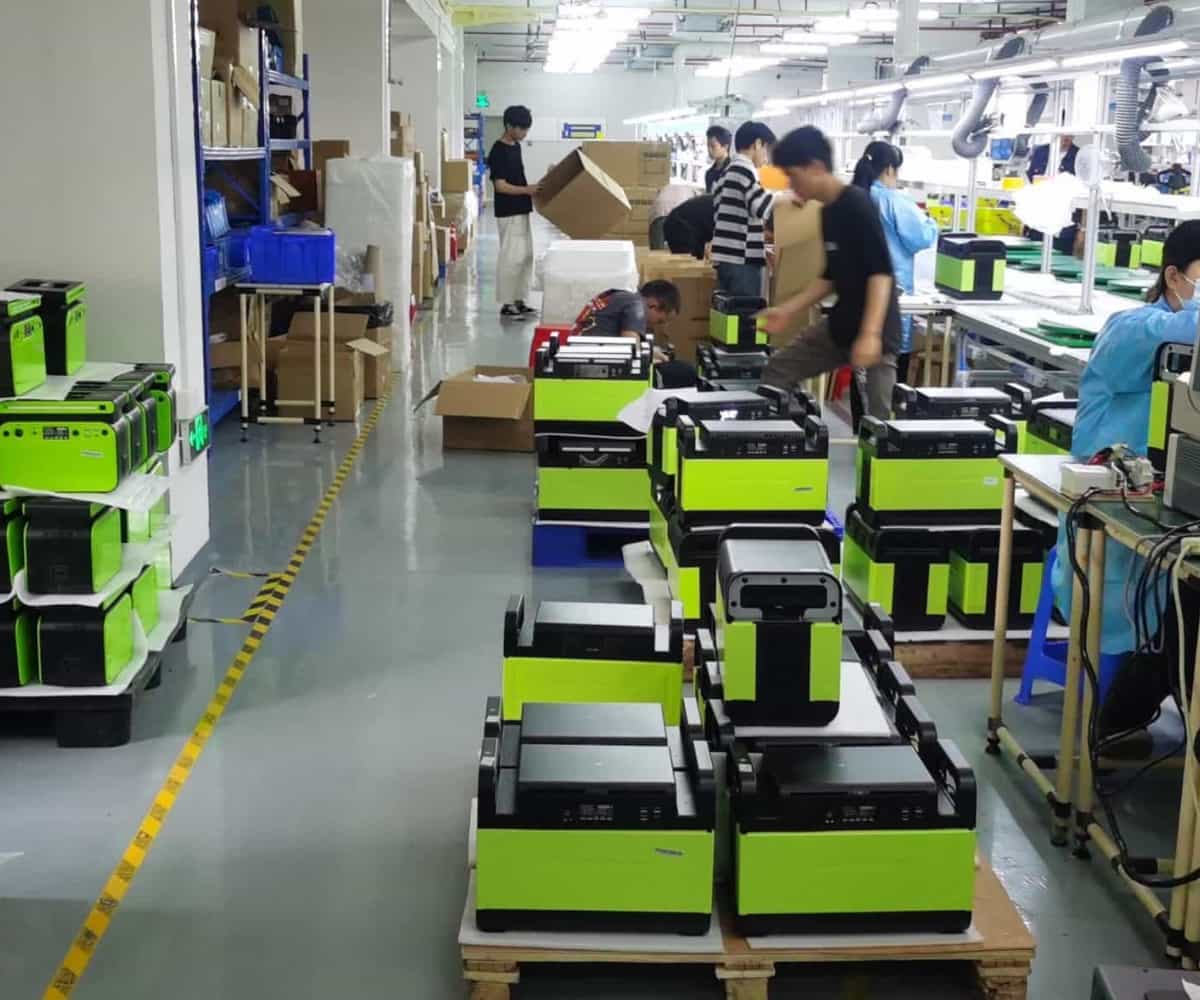 Estaciones de energía portátiles verdes apiladas en la línea de montaje final de la fábrica Piforz, listas para distribución B2B.