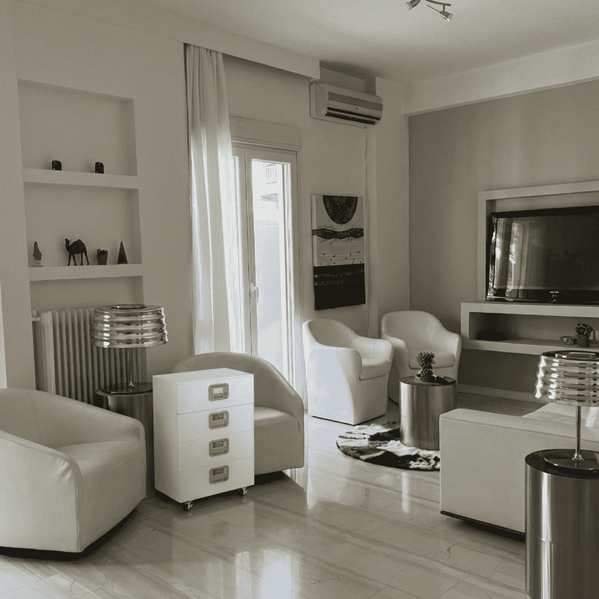 Un moderno sistema de almacenamiento de energía en baterías de color blanco con tres módulos apilables, ubicado discretamente en una sala de estar minimalista. El equipo cuenta con pantallas LCD de monitoreo y ruedas para facilitar su movilidad en interiores residenciales.