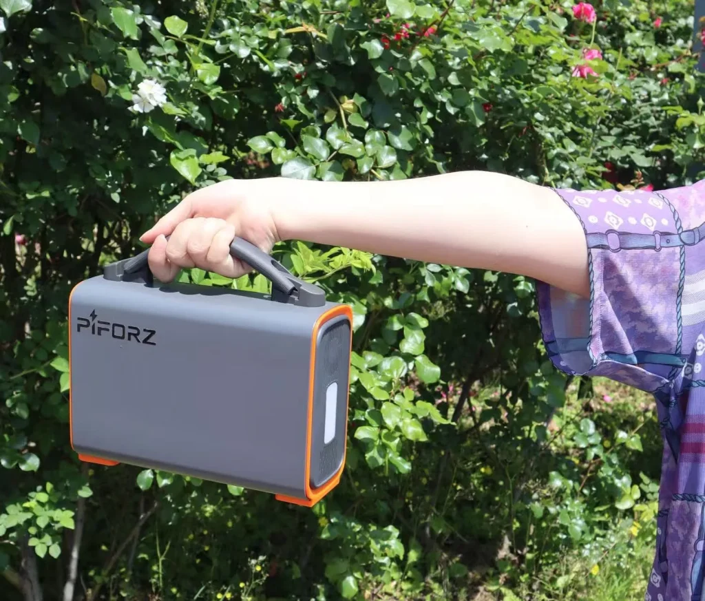 自然の中、ハンドルを持って手軽に持ち運ぶ小型ポータブル電源と側面のLEDライト。