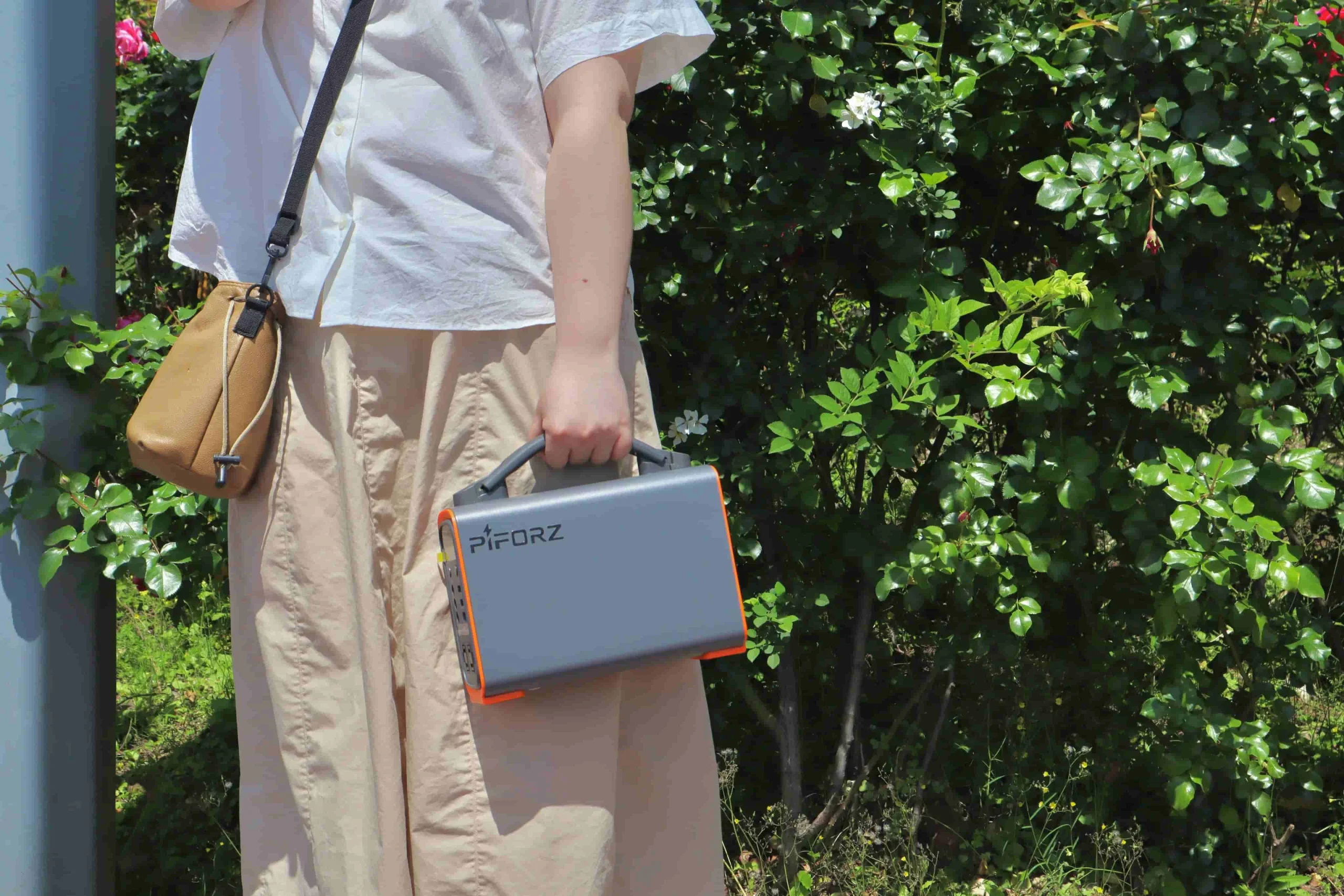 女性が片手で軽々と持ち運んでいる、グレーとオレンジカラーの小型ポータブル電源。