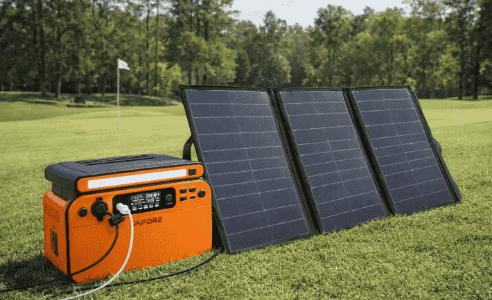 An orange Piorz portable power station connected to a 3-fold solar panel on a green grass field, demonstrating off-grid renewable energy solar charging.