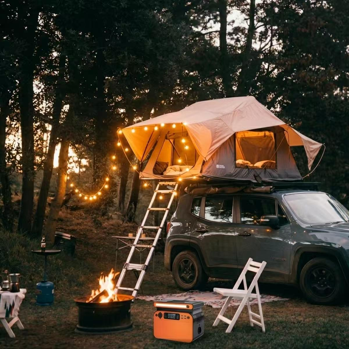 A portable power station sitting on the grass next to a campfire, providing electricity for a rooftop tent and decorative string lights on a SUV in a forest at dusk.