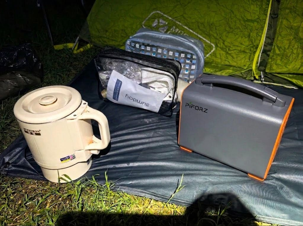 A portable battery power station operating silently at night next to a camping tent and kettle, providing pure sine wave energy for sensitive electronics.