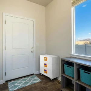 A white, modular ESS system with three stacked LiFePO4 battery modules on wheels, placed in a modern home entryway near a doorway. This portable energy storage system provides reliable backup power for residential use.