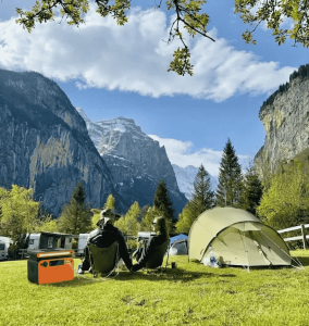 A complete portable solar panel kit with battery and inverter being used at a scenic campsite to provide silent power for lights and mobile devices.