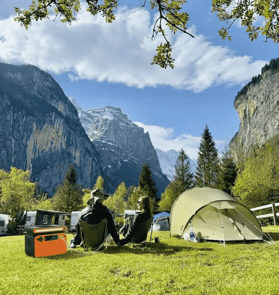 A complete portable solar panel kit with battery and inverter being used at a scenic campsite to provide silent power for lights and mobile devices.