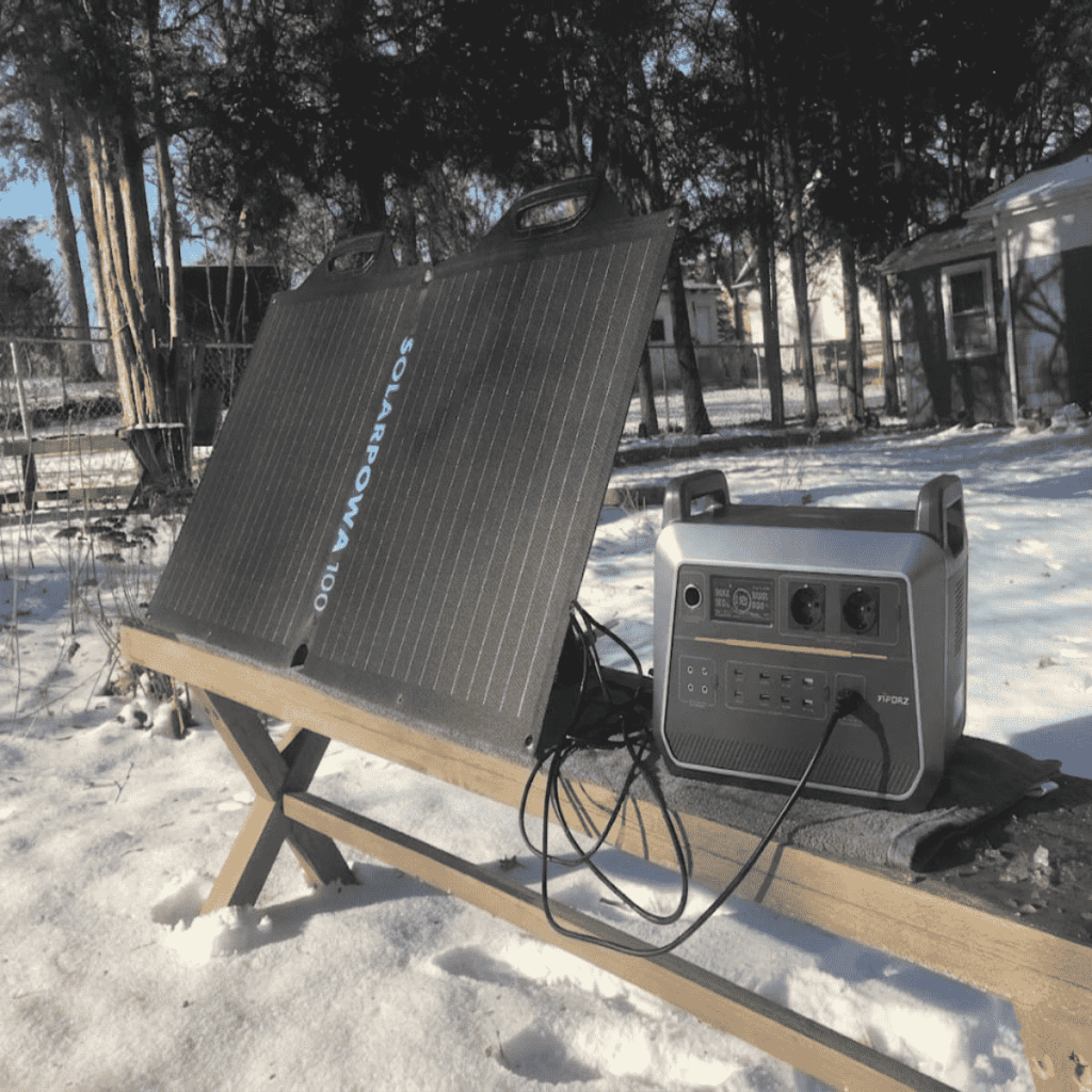 A Piforz portable solar generator connected to a 100W solar panel in a snowy outdoor setting for reliable off-grid power