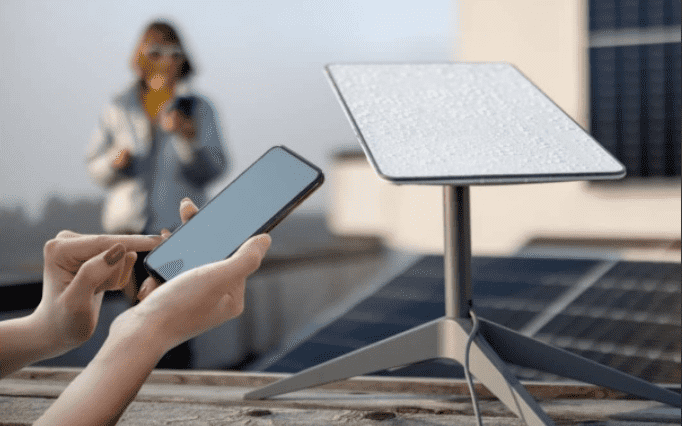 Close up of a person using a mobile phone to check connectivity next to a Starlink Mini dish on a roof with solar panels.