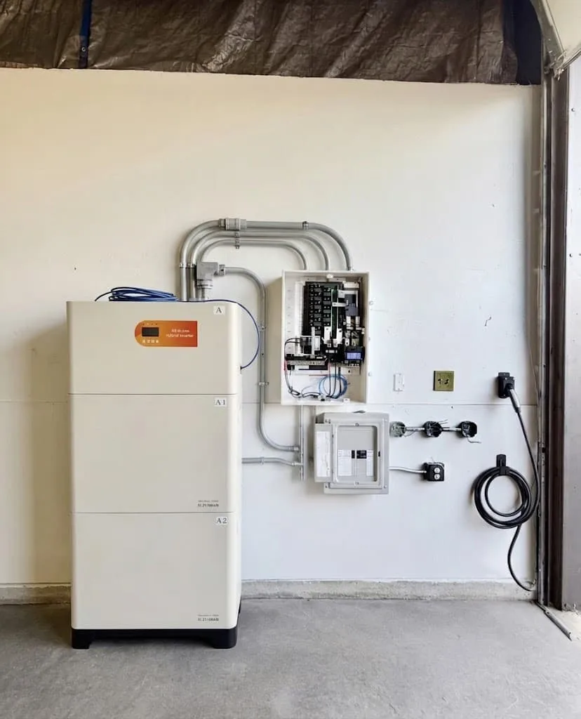 Properly wired off-grid solar energy storage system including hybrid inverter, circuit breakers, and battery bank mounted on a garage wall.