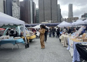 Busy outdoor craft fair and maker market with tents, vendors, and shoppers walking between display tables.