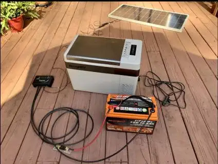 DIY solar power system with a solar panel, MPPT controller, LiFePO4 battery, and a 12V portable fridge on a wooden deck.