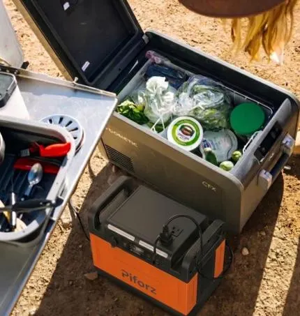 Portable solar power station plugged into an open Dometic camping fridge filled with food at a campsite.