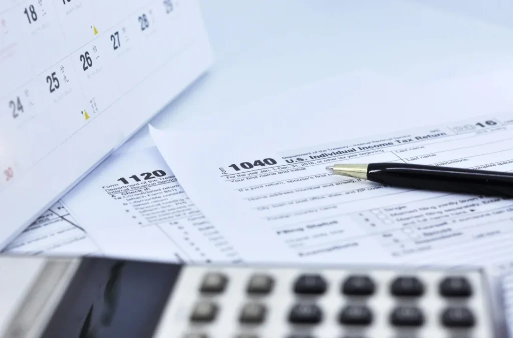 U.S. federal income tax forms, calendar, and calculator on a desk for claiming residential clean energy credits